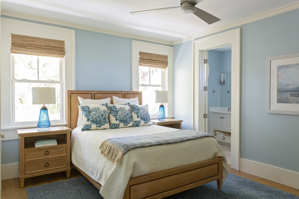 Modelo de dormitorio principal costero sin chimenea con paredes azules y suelo de madera en tonos medios