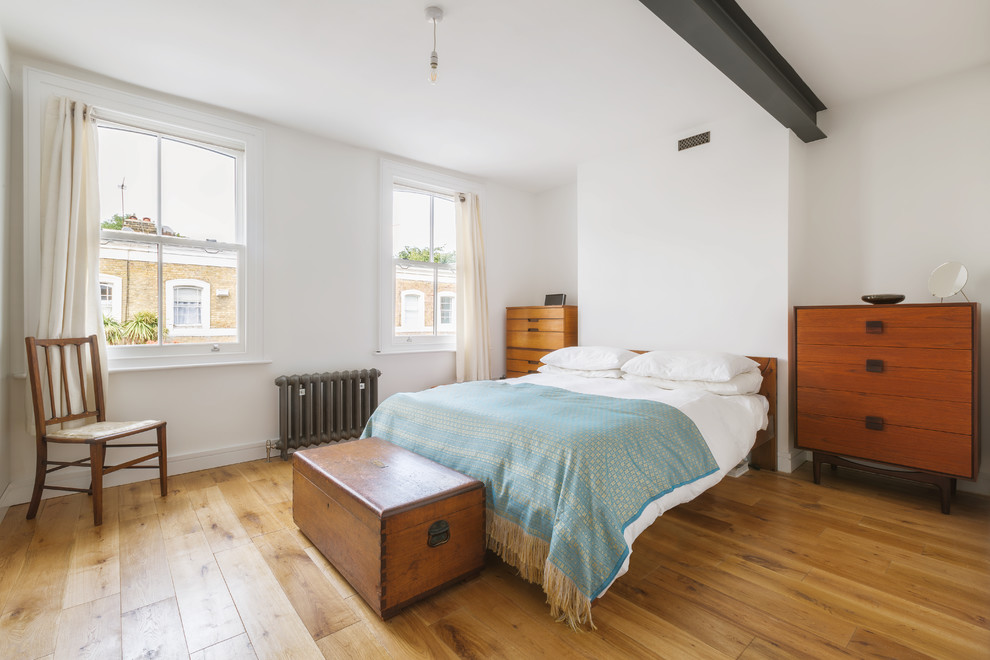Diseño de dormitorio principal contemporáneo de tamaño medio sin chimenea con paredes blancas, suelo de madera en tonos medios, marco de chimenea de yeso y suelo marrón