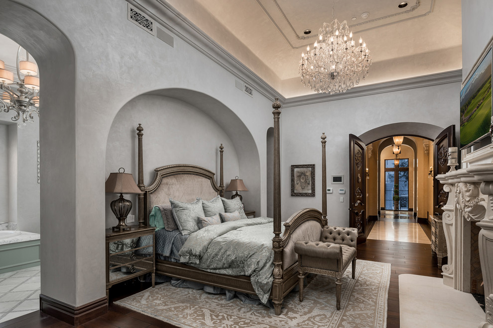 На фото: огромная хозяйская спальня в средиземноморском стиле с серыми стенами, стандартным камином, коричневым полом, полом из керамогранита, фасадом камина из камня и многоуровневым потолком