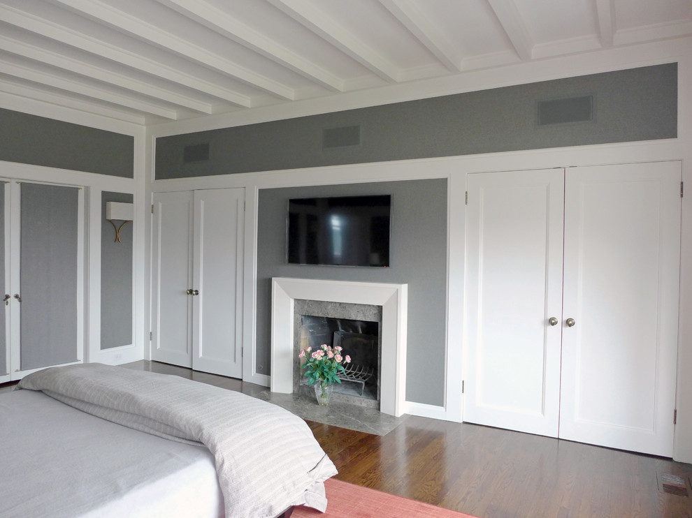 На фото: большая хозяйская спальня в стиле неоклассика (современная классика) с серыми стенами, паркетным полом среднего тона, стандартным камином, фасадом камина из камня и коричневым полом с
