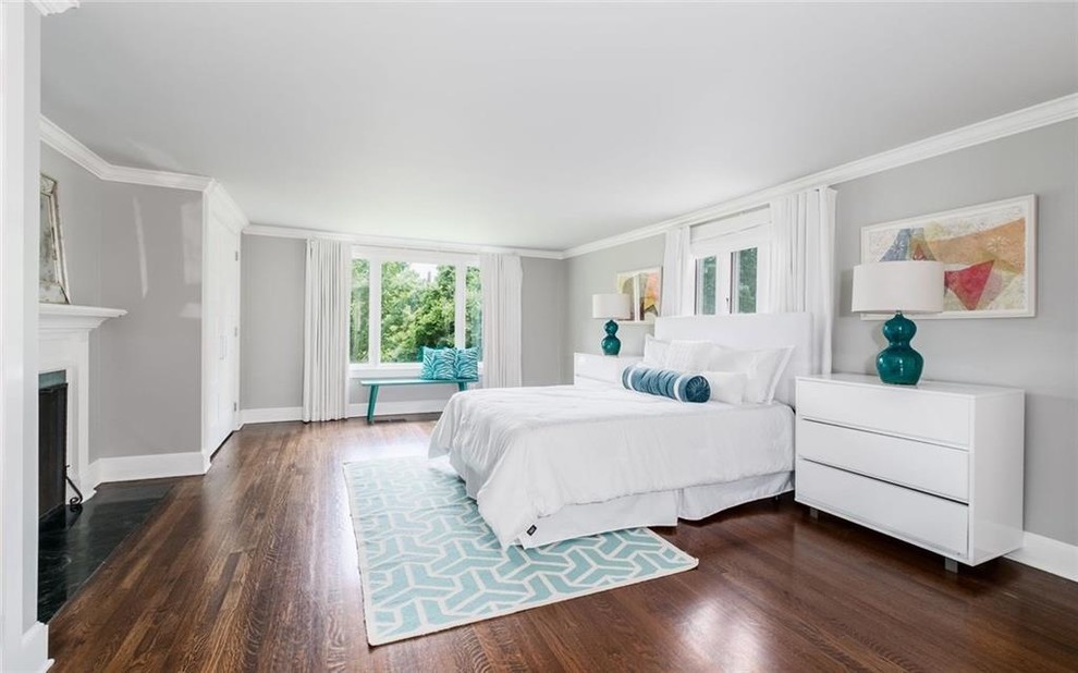 На фото: хозяйская спальня среднего размера в стиле неоклассика (современная классика) с серыми стенами, темным паркетным полом, стандартным камином, фасадом камина из дерева и коричневым полом с