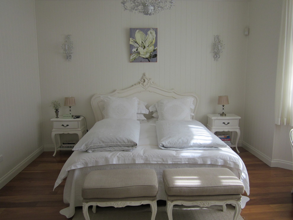 Modelo de dormitorio principal clásico de tamaño medio con paredes blancas y suelo de madera en tonos medios