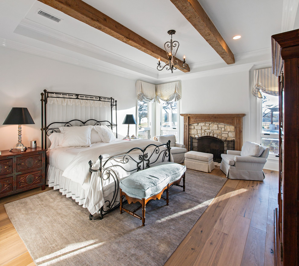 Foto de habitación de invitados rústica grande con paredes blancas, suelo de madera en tonos medios, todas las chimeneas y marco de chimenea de piedra