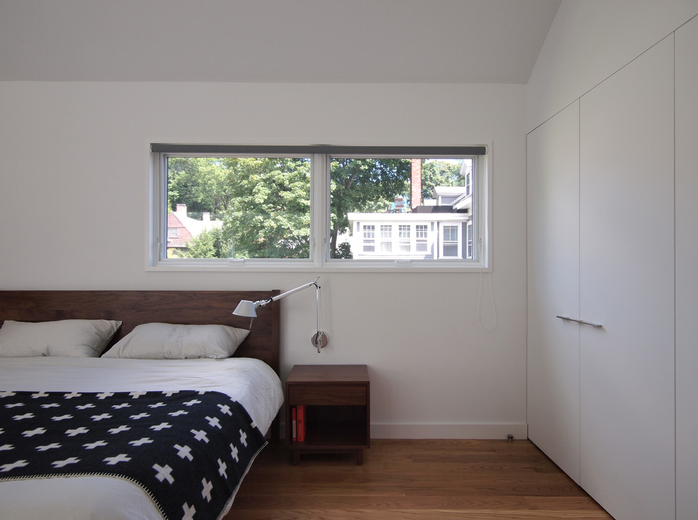 Réalisation d'une chambre parentale minimaliste avec un mur blanc, un sol en bois brun et aucune cheminée.