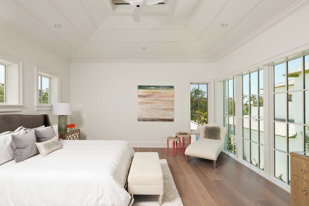 Modelo de dormitorio principal tropical sin chimenea con paredes blancas y suelo de madera en tonos medios