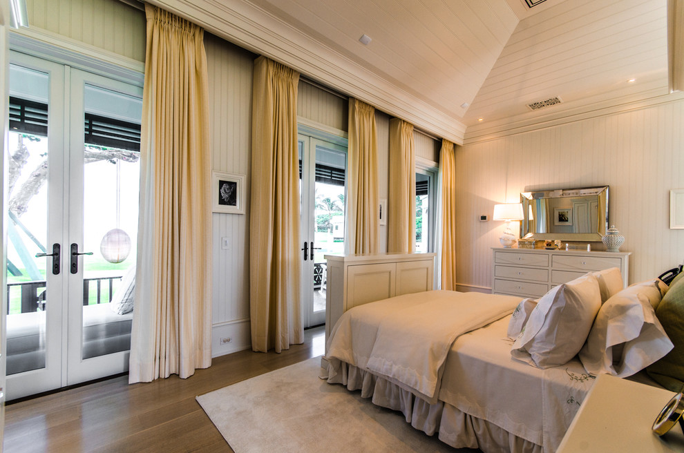Immagine di una grande camera degli ospiti tropicale con pareti bianche e pavimento in legno massello medio