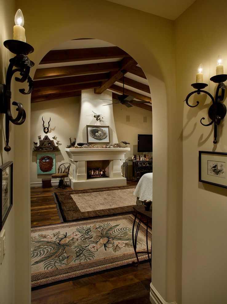 フェニックスにある広い地中海スタイルのおしゃれな主寝室 (ベージュの壁、濃色無垢フローリング、標準型暖炉、漆喰の暖炉まわり)