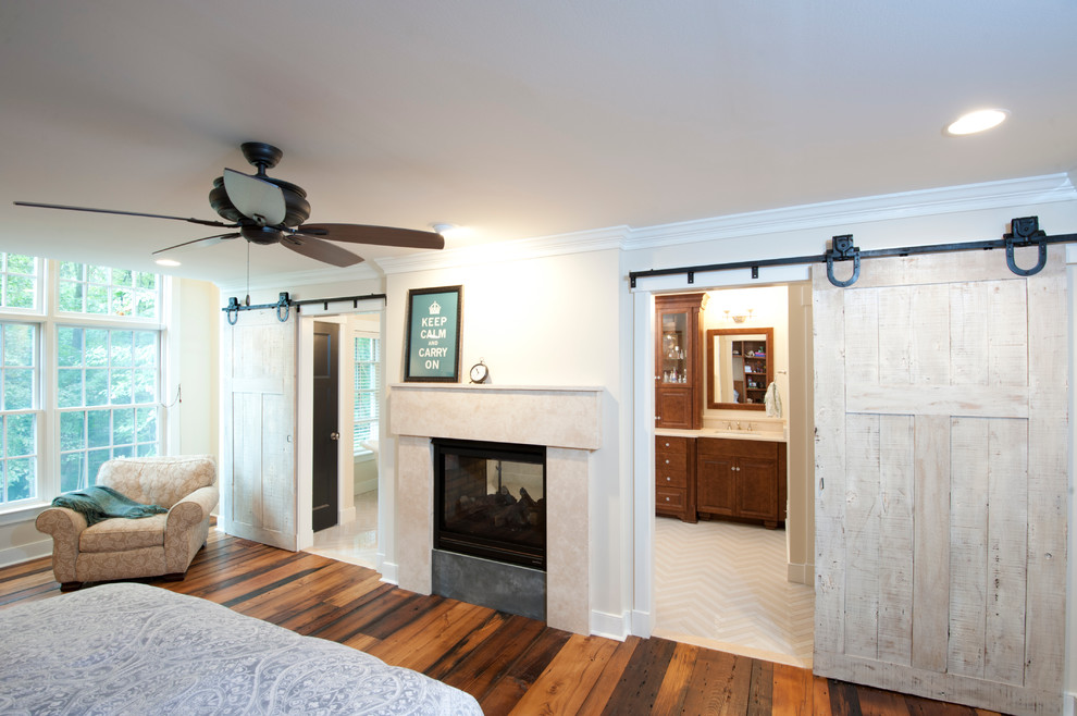 This is an example of a large rustic master bedroom in Baltimore with white walls, dark hardwood flooring, a standard fireplace, a concrete fireplace surround and brown floors.