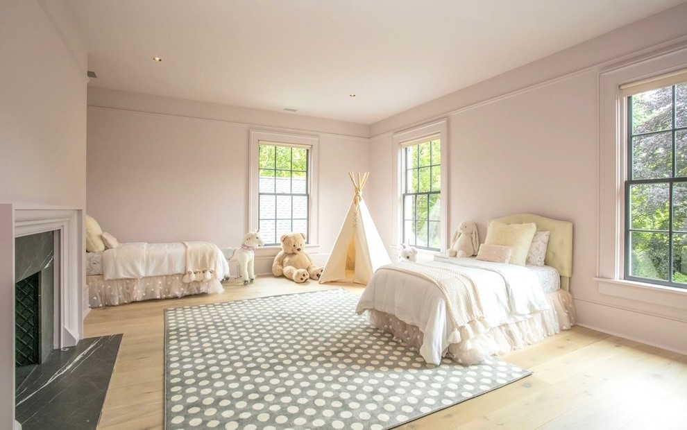 Modelo de dormitorio tradicional renovado con paredes rosas, suelo de madera clara, todas las chimeneas, marco de chimenea de piedra y suelo beige