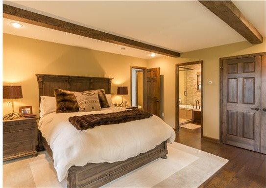 Modelo de dormitorio principal rural de tamaño medio con paredes beige y suelo de madera en tonos medios