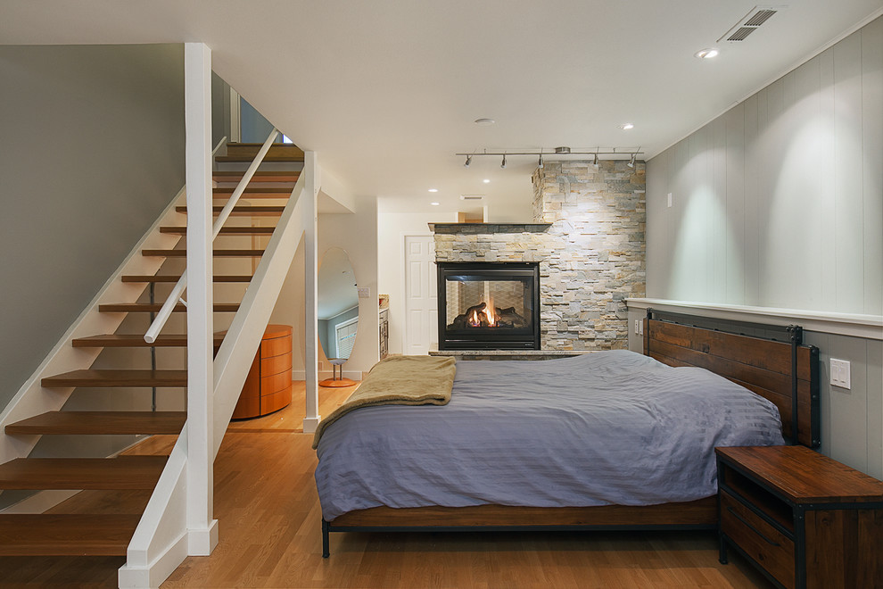 На фото: хозяйская спальня среднего размера в стиле неоклассика (современная классика) с серыми стенами, паркетным полом среднего тона, фасадом камина из камня и двусторонним камином