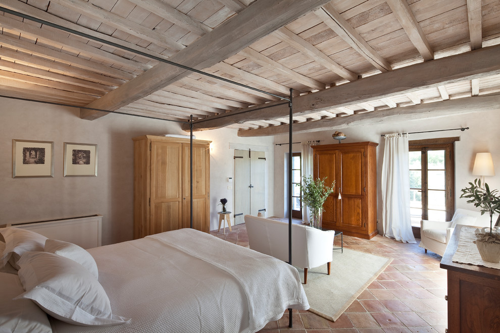 Стильный дизайн: спальня в средиземноморском стиле с бежевыми стенами, полом из терракотовой плитки и красным полом - последний тренд