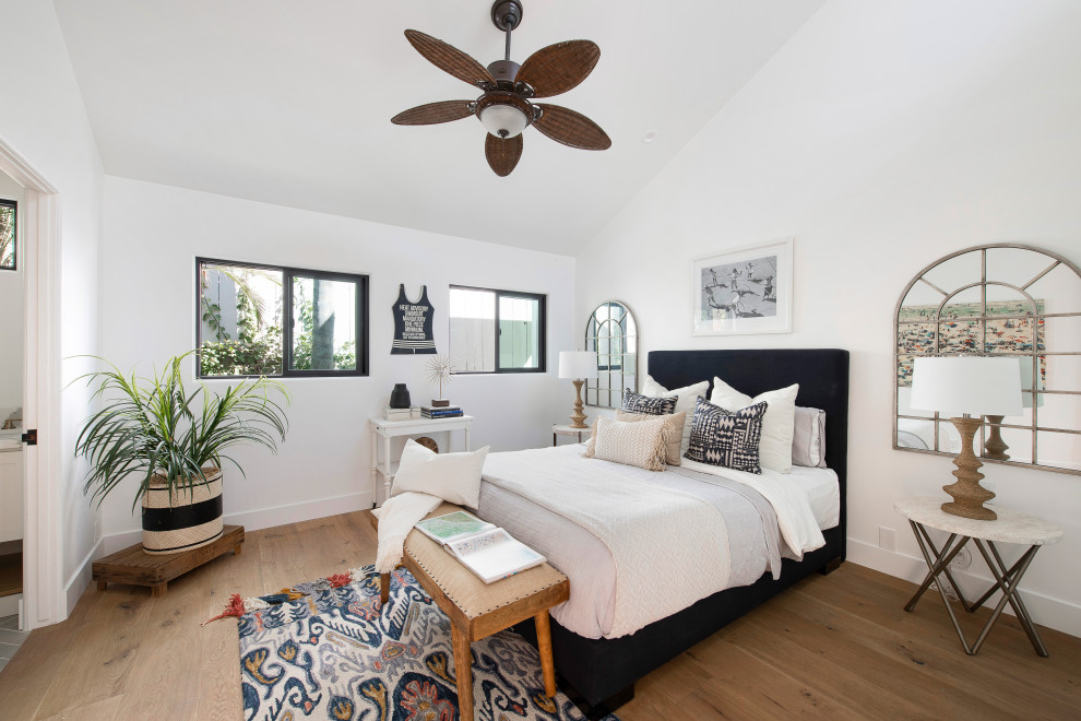 Example of a beach style guest medium tone wood floor, brown floor and vaulted ceiling bedroom design in Orange County with white walls