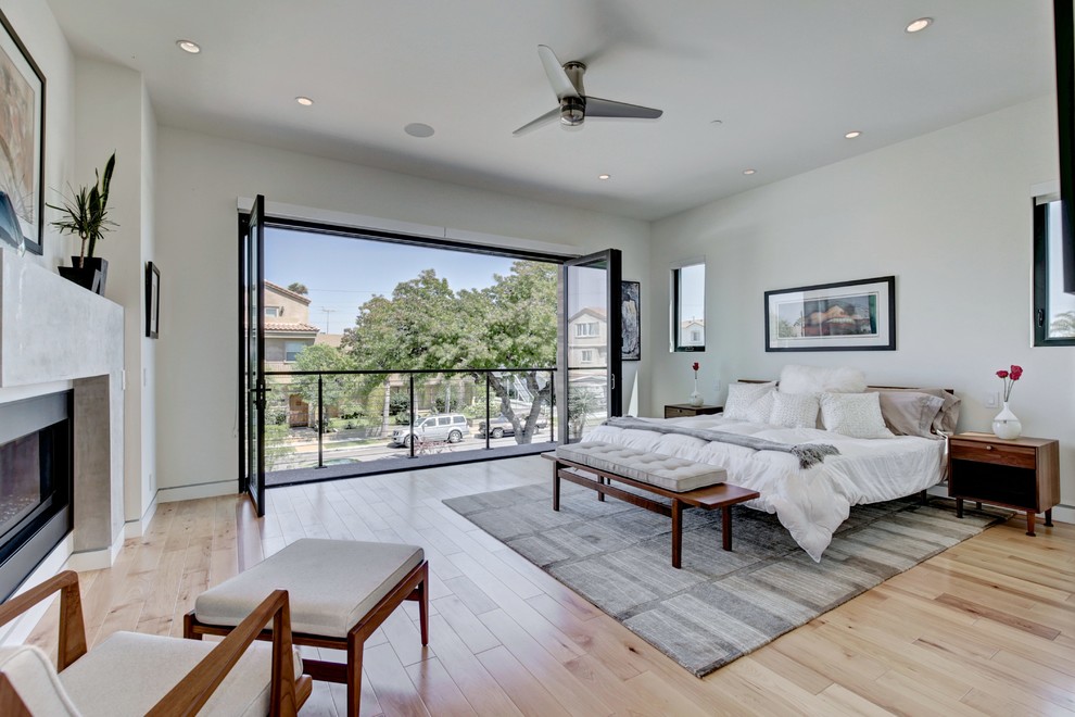 Modernes Hauptschlafzimmer mit grauer Wandfarbe, hellem Holzboden, Gaskamin, Kaminumrandung aus Beton und beigem Boden in San Diego