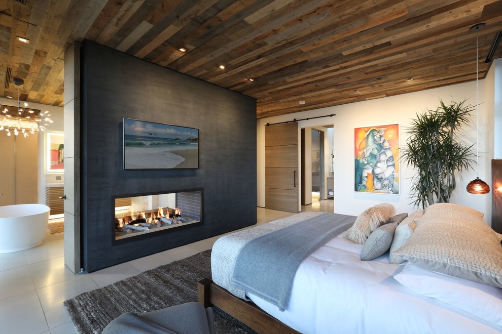 Imagen de dormitorio principal contemporáneo con paredes blancas, chimenea de doble cara y suelo gris