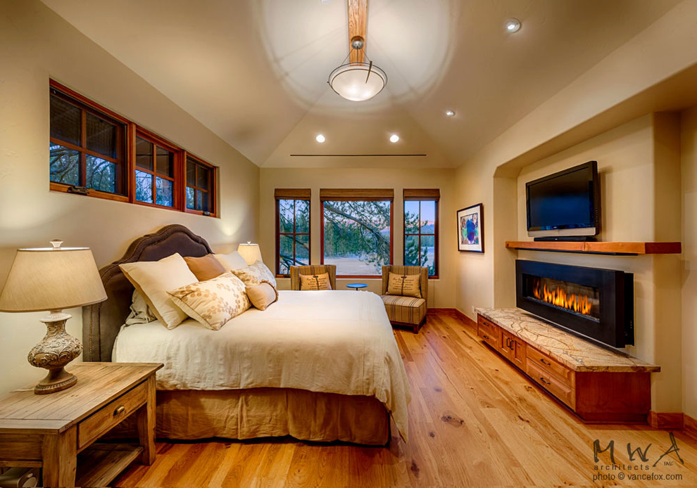 Modelo de dormitorio principal rural grande con paredes beige, suelo de madera clara, chimenea lineal y marco de chimenea de metal