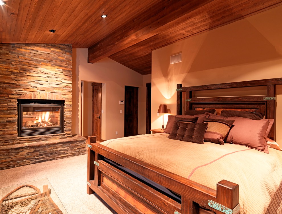 Diseño de dormitorio rústico con paredes beige, moqueta, todas las chimeneas y marco de chimenea de piedra