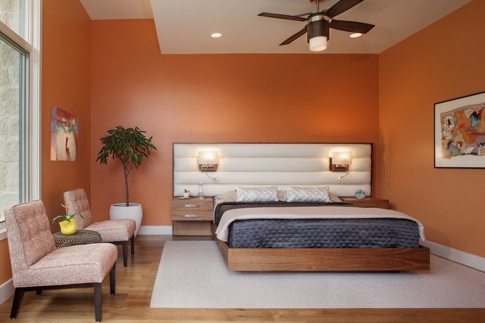 Réalisation d'une grande chambre parentale design avec un mur orange, un sol en bois brun, un sol marron et aucune cheminée.