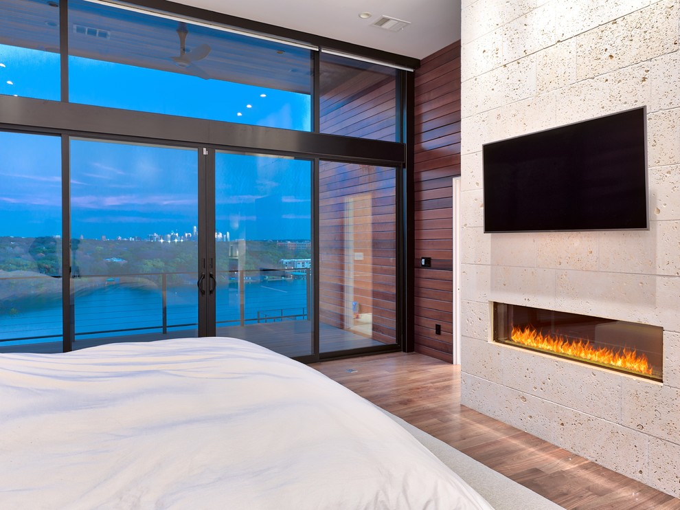 Modernes Hauptschlafzimmer mit weißer Wandfarbe, braunem Holzboden, Kaminumrandung aus Stein und braunem Boden in Austin