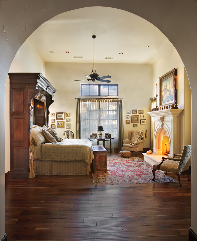 Mediterranes Hauptschlafzimmer mit beiger Wandfarbe, dunklem Holzboden, Kamin und Kaminumrandung aus Stein in Austin