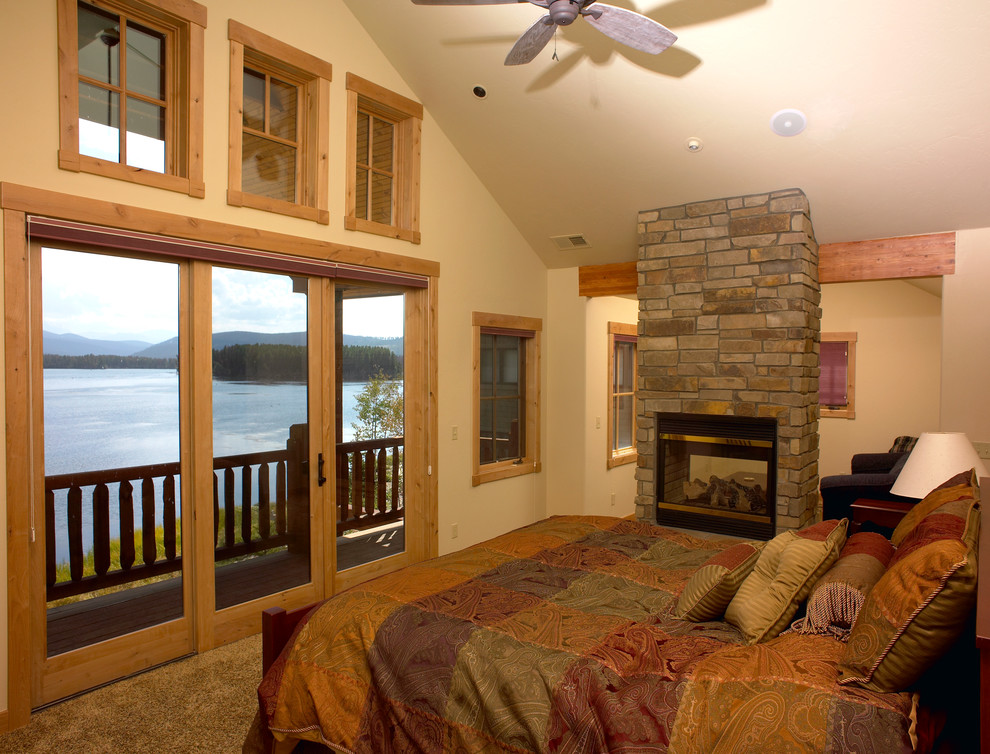Diseño de dormitorio principal de estilo americano con moqueta, chimenea de doble cara y marco de chimenea de piedra