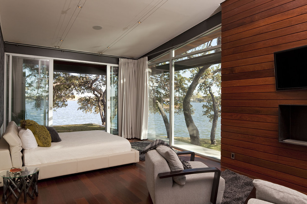 Пример оригинального дизайна: большая хозяйская спальня в современном стиле с темным паркетным полом, серыми стенами, горизонтальным камином и фасадом камина из дерева