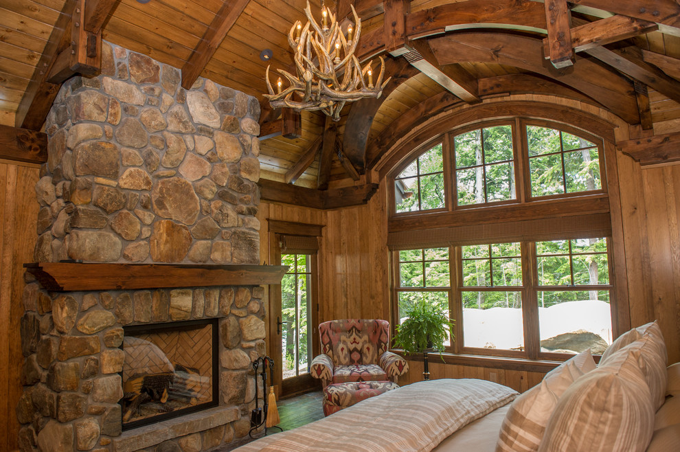 Aménagement d'une chambre parentale craftsman avec un sol en bois brun, une cheminée standard et un manteau de cheminée en pierre.
