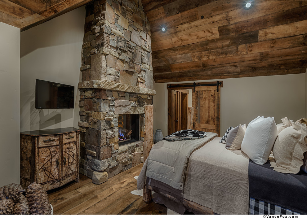 Exemple d'une chambre parentale montagne de taille moyenne avec un mur beige, un sol en bois brun, une cheminée standard et un manteau de cheminée en pierre.