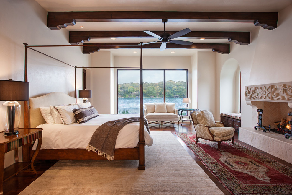 Photo of a large traditional master bedroom in Austin with white walls, medium hardwood flooring, a standard fireplace and a plastered fireplace surround.