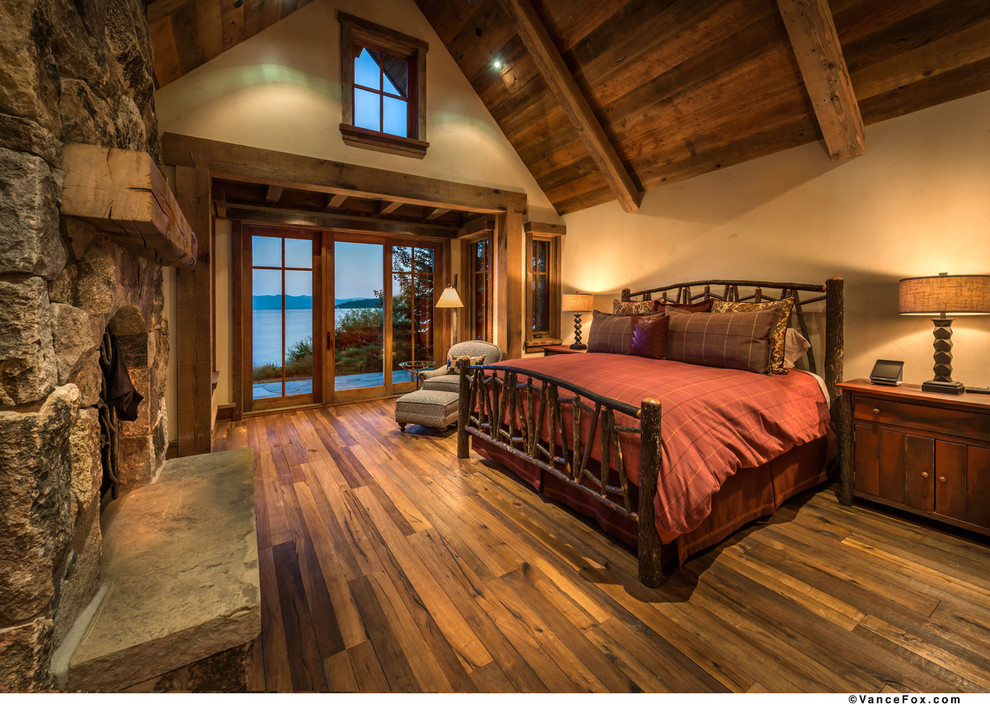 Diseño de dormitorio principal de estilo americano grande con paredes beige, suelo de madera en tonos medios, marco de chimenea de piedra y todas las chimeneas