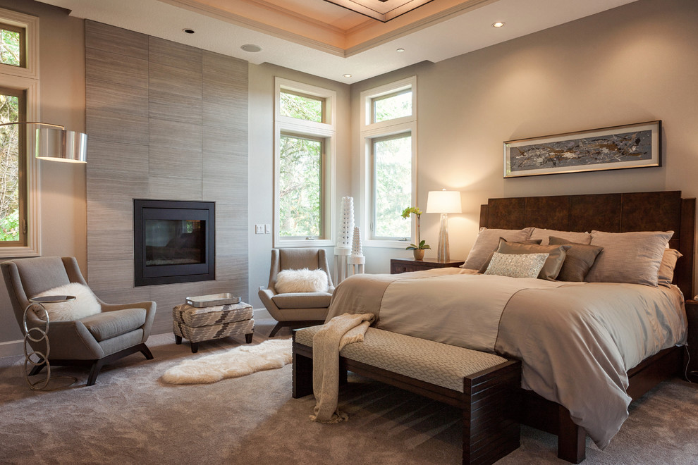 Idée de décoration pour une chambre chalet avec un mur beige, une cheminée standard, un manteau de cheminée en pierre et un sol gris.