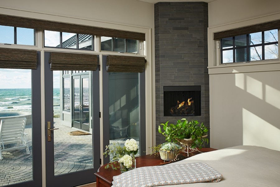 グランドラピッズにあるトランジショナルスタイルのおしゃれな寝室 (グレーの壁、無垢フローリング、コーナー設置型暖炉、石材の暖炉まわり、茶色い床)