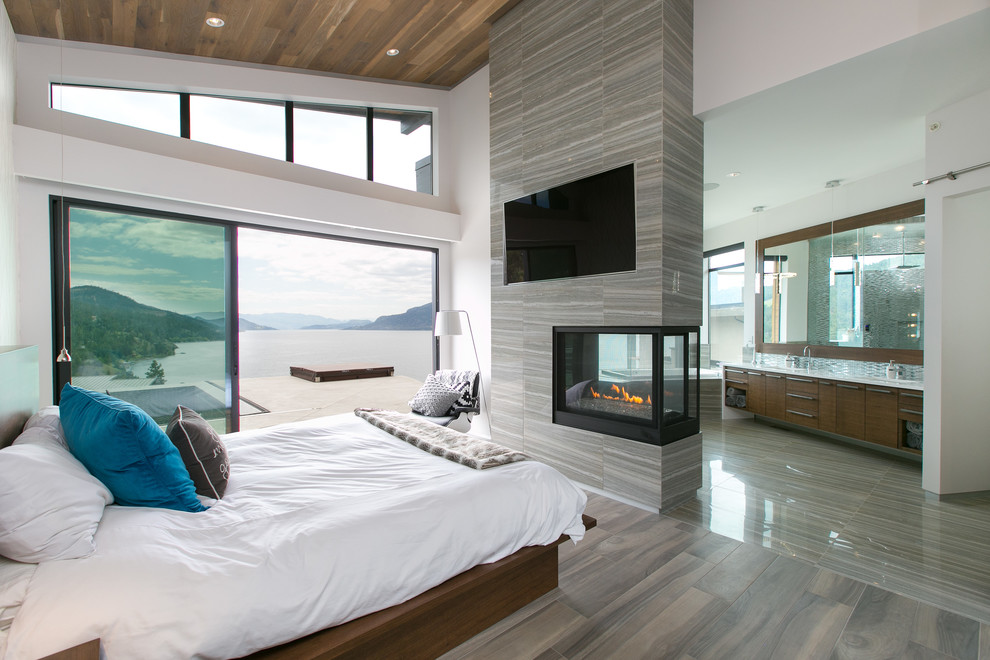Modernes Hauptschlafzimmer mit grauer Wandfarbe, Porzellan-Bodenfliesen, gefliester Kaminumrandung und Tunnelkamin in Vancouver