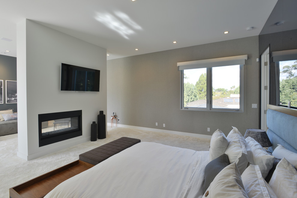 This is an example of a large modern master bedroom in Los Angeles with grey walls, carpet, a metal fireplace surround and a two-sided fireplace.