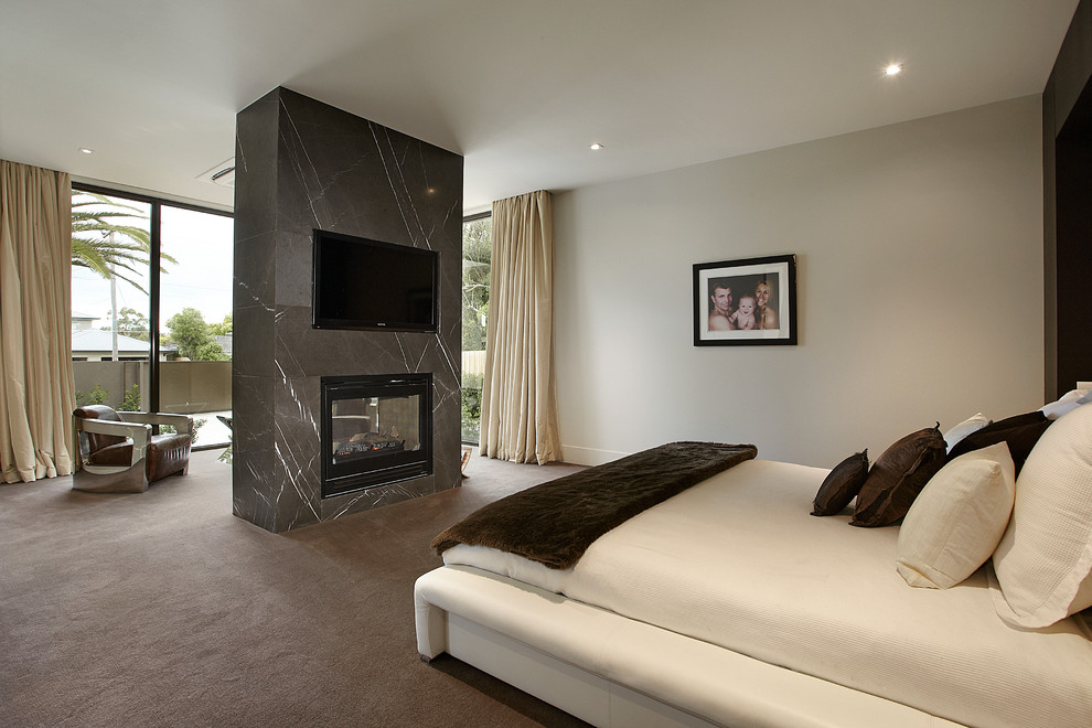 Large contemporary bedroom in Melbourne with white walls, carpet, a stone fireplace surround and a two-sided fireplace.