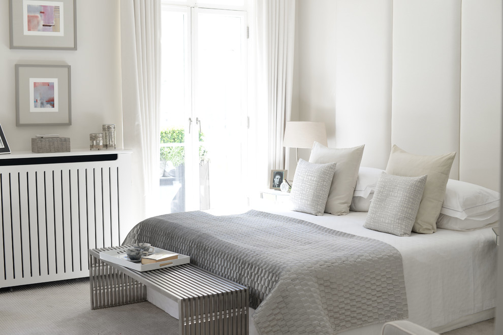 This is an example of a contemporary grey and cream bedroom in London with white walls and carpet.