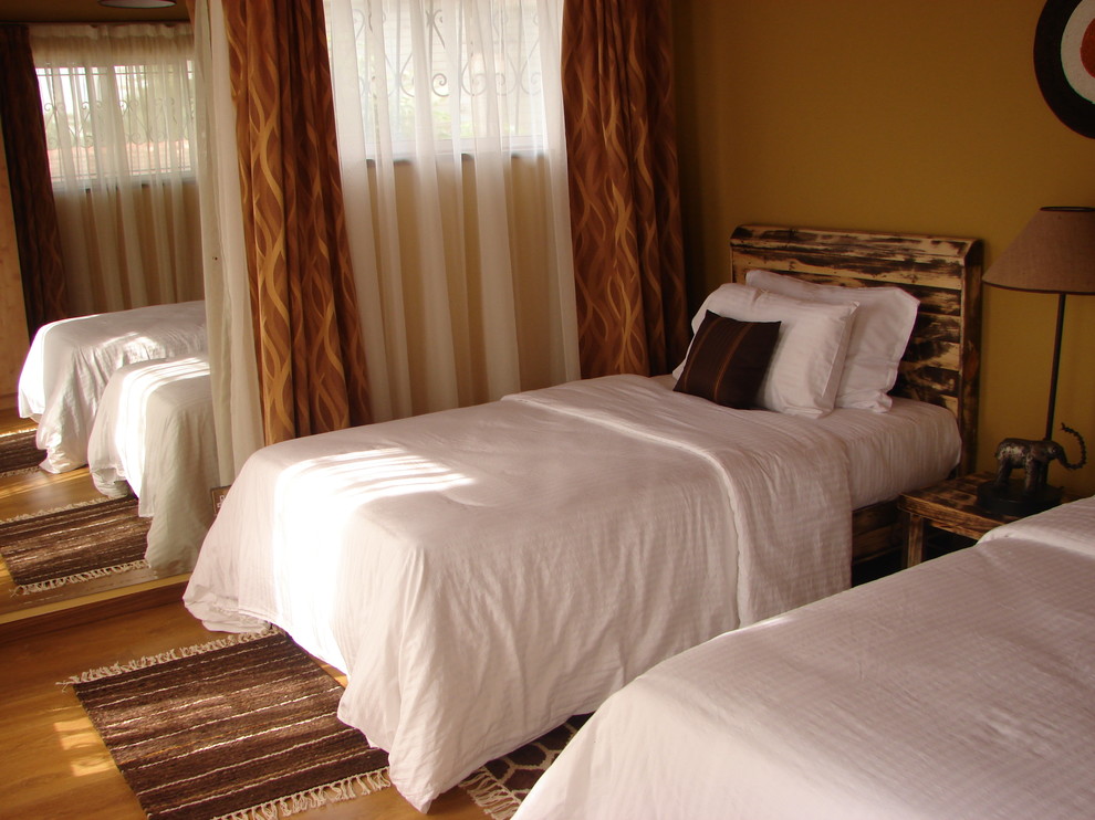 Ejemplo de habitación de invitados tropical sin chimenea con paredes marrones y suelo laminado