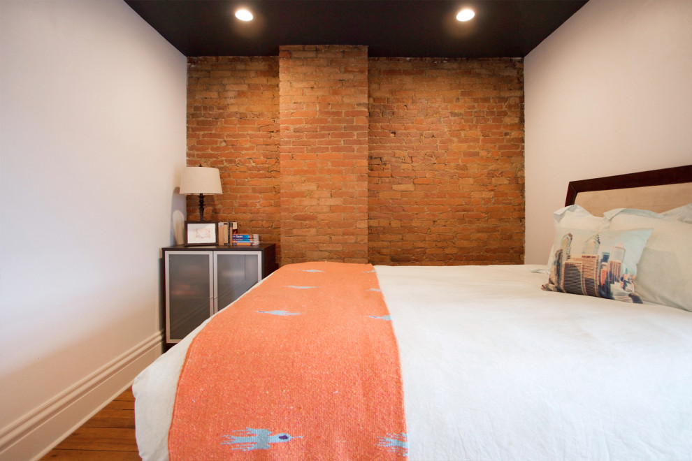 Diseño de habitación de invitados tradicional renovada pequeña con paredes blancas, suelo de madera en tonos medios y ladrillo