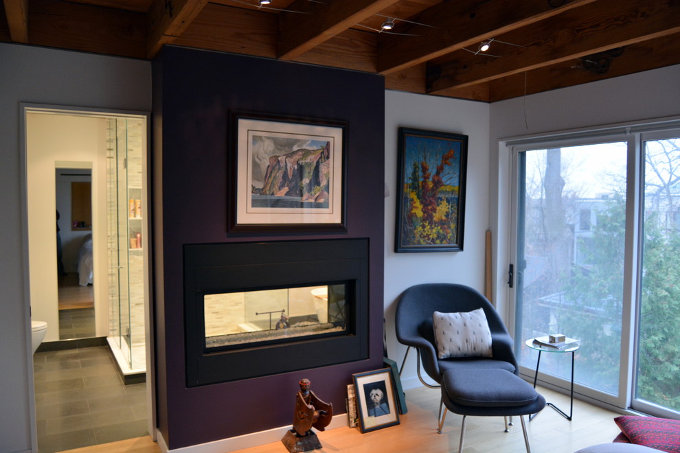 Cette photo montre une chambre parentale tendance de taille moyenne avec un mur violet, parquet clair, une cheminée double-face et un manteau de cheminée en métal.