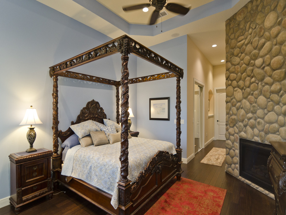 Ejemplo de dormitorio principal grande con paredes azules, suelo de madera oscura, todas las chimeneas y marco de chimenea de piedra