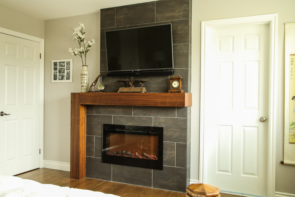 Example of a mid-sized transitional master medium tone wood floor and brown floor bedroom design in Edmonton with gray walls, a ribbon fireplace and a tile fireplace