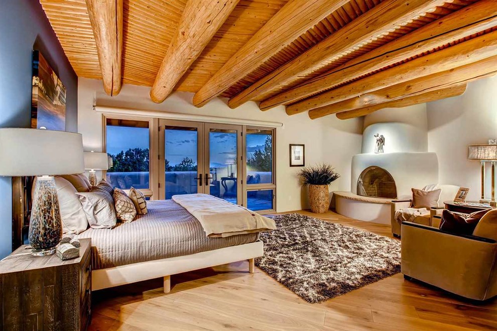 Cette photo montre une grande chambre parentale sud-ouest américain avec une cheminée d'angle, un mur bleu, un sol en bois brun et un manteau de cheminée en plâtre.