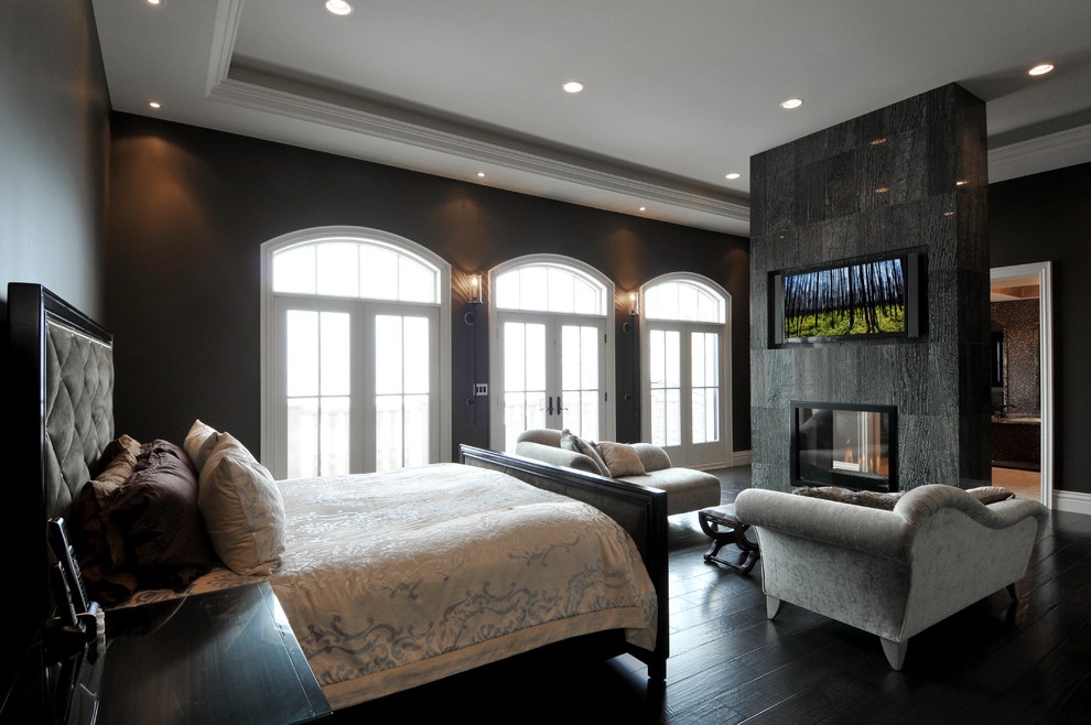 Свежая идея для дизайна: большая хозяйская спальня в стиле неоклассика (современная классика) с черными стенами, деревянным полом, подвесным камином, фасадом камина из камня и черным полом - отличное фото интерьера