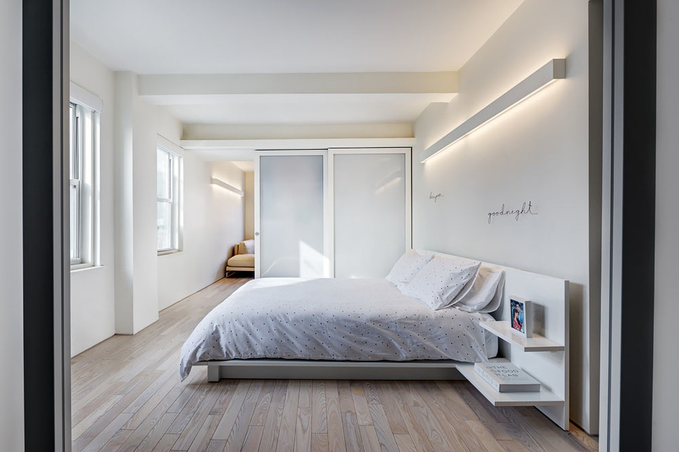 This is an example of a medium sized modern bedroom in New York with white walls, light hardwood flooring and no fireplace.