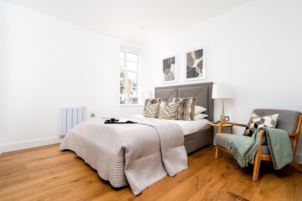 This is an example of a contemporary bedroom in London with white walls, medium hardwood flooring and brown floors.