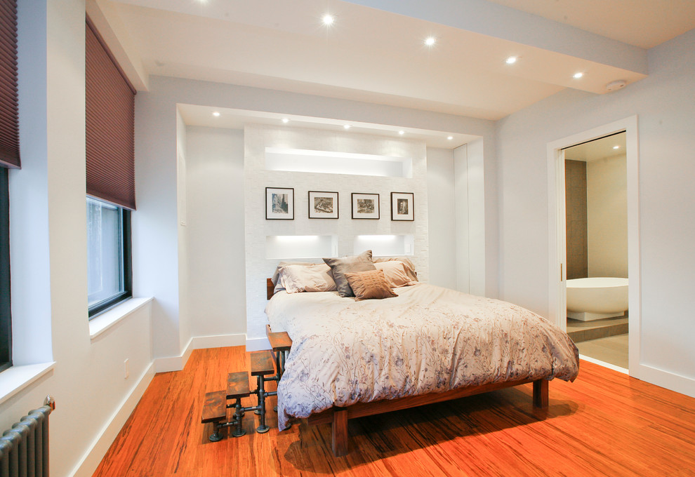 Modelo de dormitorio principal actual de tamaño medio con paredes blancas y suelo de madera en tonos medios