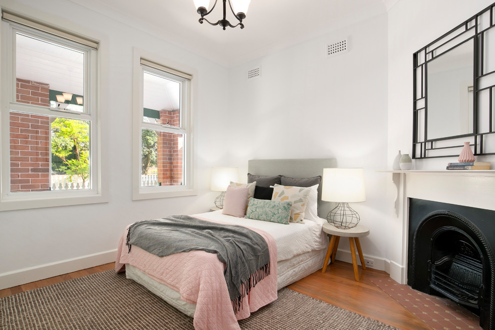 シドニーにある小さなトランジショナルスタイルのおしゃれな寝室 (無垢フローリング、コーナー設置型暖炉、白い壁、茶色い床、漆喰の暖炉まわり、グレーとブラウン) のインテリア