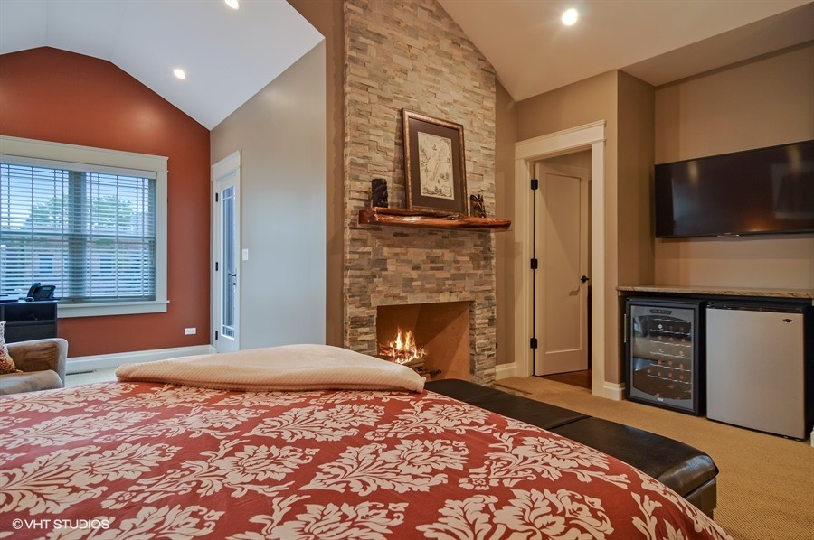 Idées déco pour une grande chambre craftsman avec un mur rouge, une cheminée standard, un manteau de cheminée en pierre et un sol beige.