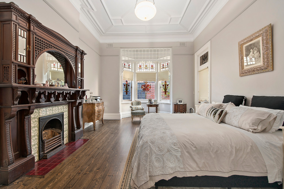 Klassisches Hauptschlafzimmer mit beiger Wandfarbe, dunklem Holzboden, gefliester Kaminumrandung und Kamin in Melbourne