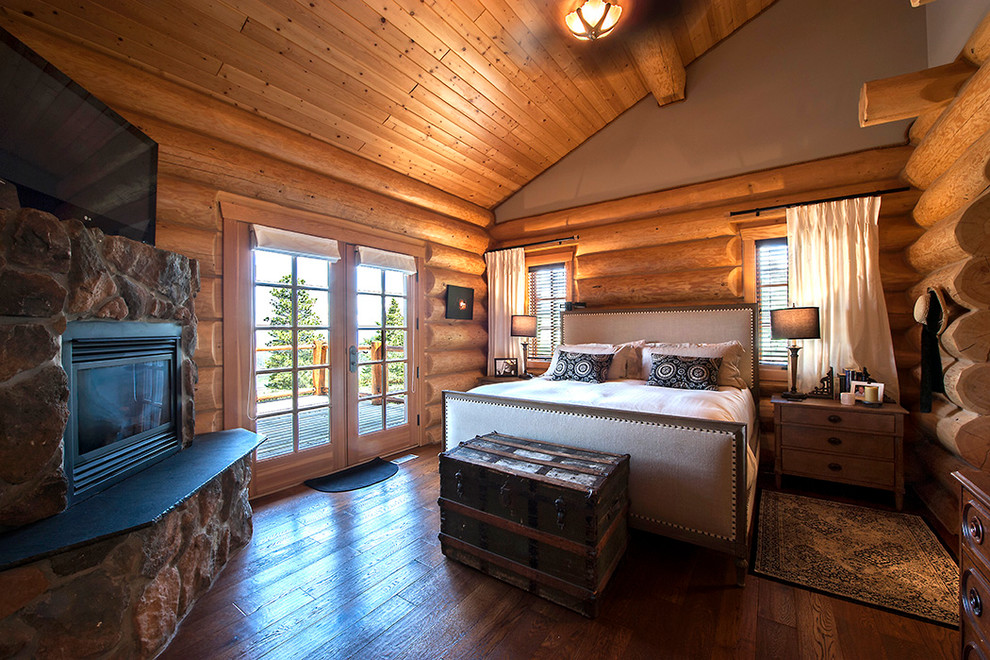 Imagen de dormitorio principal rural grande con paredes marrones, suelo de madera oscura, todas las chimeneas y marco de chimenea de piedra
